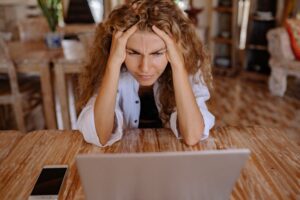 Distressed woman leaning on a wooden table, her furrowed brow and worried expression symbolizing a customer experiencing a pain point in the business environment, in dire need of an effective solution.